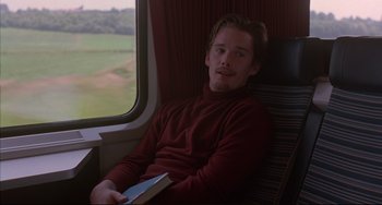 Movie still from “Before Sunrise” (1995), directed by Richard Linklater – A man sitting in a chair holding a book; Medium shot, High angle