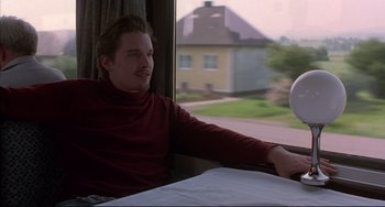 Movie still from “Before Sunrise” (1995), directed by Richard Linklater – A man sitting in front of a window with his arms crossed; Medium shot, Low angle