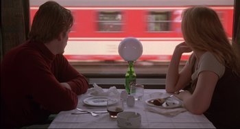 Movie still from “Before Sunrise” (1995), directed by Richard Linklater – Two people sitting at a dinner table with a train in the background; Medium shot, Over the shoulder angle
