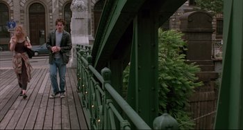Movie still from “Before Sunrise” (1995), directed by Richard Linklater – A man standing on a wooden bridge near a bush; Wide shot, Low angle