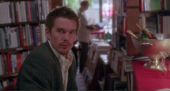 Movie still from “Before Sunset” (2004), directed by Richard Linklater – A man sitting in front of a bunch of books in a room; Medium shot, Over the shoulder angle