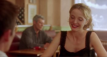 Movie still from “Before Sunset” (2004), directed by Richard Linklater – A woman sitting at a table with a man in the background; Close Up shot, Over the shoulder angle