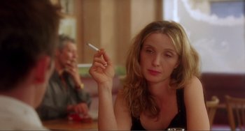 Movie still from “Before Sunset” (2004), directed by Richard Linklater – A woman sitting at a table holding a cigarette in her hand; Close Up shot, Over the shoulder angle