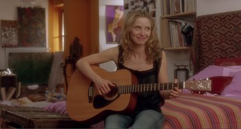 Movie still from “Before Sunset” (2004), directed by Richard Linklater – A woman sitting on a bed holding a guitar; Medium shot, Over the shoulder angle