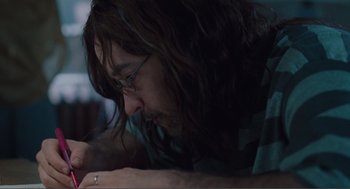 Movie still from “Being John Malkovich” (1999), directed by Spike Jonze – A man with long brown hair is writing on a paper; Close Up shot, Low angle