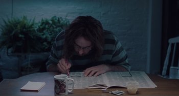 Movie still from “Being John Malkovich” (1999), directed by Spike Jonze – A man sitting at a table writing on a newspaper; Medium shot, High angle