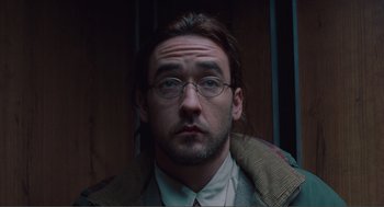 Movie still from “Being John Malkovich” (1999), directed by Spike Jonze – A person wearing glasses and a jacket; Close Up shot, High angle