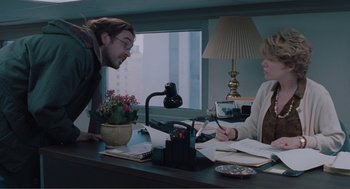 Movie still from “Being John Malkovich” (1999), directed by Spike Jonze – A man and a woman sitting at a desk with papers; Medium shot, Over the shoulder angle