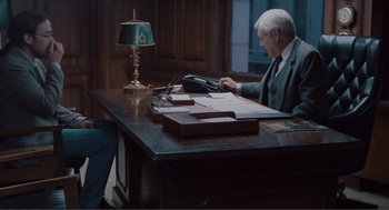 Movie still from “Being John Malkovich” (1999), directed by Spike Jonze – An older man sitting at a desk looking at a phone; Wide shot, High angle