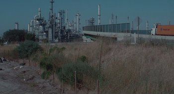 Movie still from “Being John Malkovich” (1999), directed by Spike Jonze – An oil refinery is seen in the distance behind a field; Extreme Wide shot, High angle