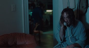 Movie still from “Being John Malkovich” (1999), directed by Spike Jonze – A man sitting on a chair talking on a phone; Medium shot, Low angle