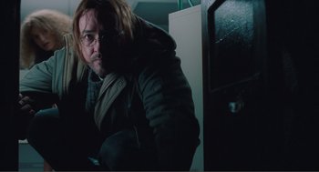 Movie still from “Being John Malkovich” (1999), directed by Spike Jonze – A man with a beard and glasses in a dark room; Medium shot, Low angle