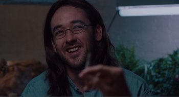 Movie still from “Being John Malkovich” (1999), directed by Spike Jonze – A man with long hair and glasses is smiling; Close Up shot, Over the shoulder angle
