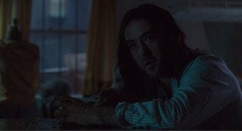 Movie still from “Being John Malkovich” (1999), directed by Spike Jonze – A man with long black hair sitting on a bed; Close Up shot, Over the shoulder angle