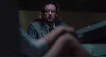 Movie still from “Being John Malkovich” (1999), directed by Spike Jonze – A man in a suit and tie sitting in front of a wall; Close Up shot, Over the shoulder angle
