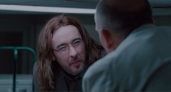 Movie still from “Being John Malkovich” (1999), directed by Spike Jonze – A man with long brown hair and glasses looking at himself in the mirror; Close Up shot, Over the shoulder angle