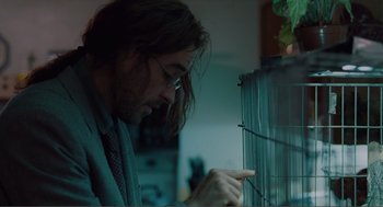 Movie still from “Being John Malkovich” (1999), directed by Spike Jonze – A man with long brown hair looking at a bird cage; Close Up shot, Low angle