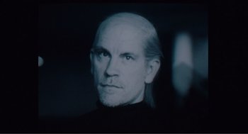 Movie still from “Being John Malkovich” (1999), directed by Spike Jonze – A black and white photo of a man with a bald head; Close Up shot, Over the shoulder angle