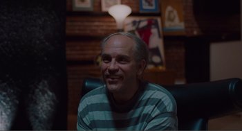 Movie still from “Being John Malkovich” (1999), directed by Spike Jonze – A man sitting in front of a lamp in a room; Close Up shot, Over the shoulder angle