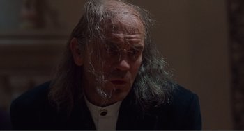 Movie still from “Being John Malkovich” (1999), directed by Spike Jonze – An old man with long white hair and wearing a black suit; Close Up shot, Over the shoulder angle