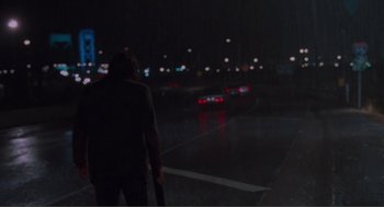 Movie still from “Being John Malkovich” (1999), directed by Spike Jonze – A man standing on the side of a road at night; Wide shot, Over the shoulder angle