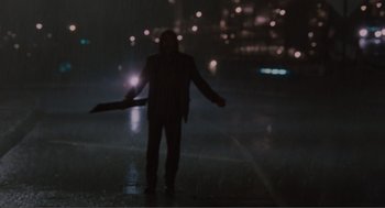 Movie still from “Being John Malkovich” (1999), directed by Spike Jonze – A man standing in the middle of the street at night holding an umbrella; Wide shot, Over the shoulder angle