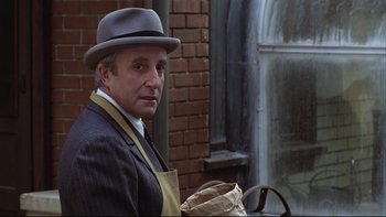 Movie still from “Being There” (1979), directed by Hal Ashby – A man in a hat and apron holding a paper bag; Close Up shot, Over the shoulder angle