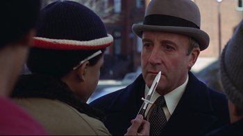 Movie still from “Being There” (1979), directed by Hal Ashby – A man in a suit and a hat holding a pair of scissors; Close Up shot, Over the shoulder angle