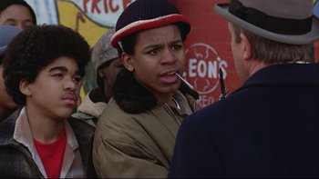 Movie still from “Being There” (1979), directed by Hal Ashby – A young man smoking a cigarette in front of two other people; Close Up shot, Over the shoulder angle