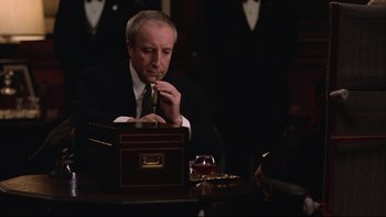 Movie still from “Being There” (1979), directed by Hal Ashby – A man sitting at a table in a suit and tie; Medium shot, Over the shoulder angle