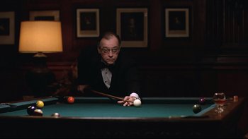 Movie still from “Being There” (1979), directed by Hal Ashby – A man in a black suit and white shirt playing a game of billiards; Medium shot, Over the shoulder angle