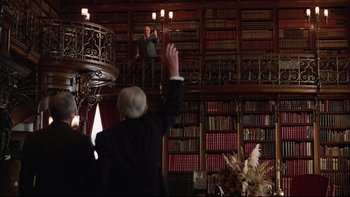 Movie still from “Being There” (1979), directed by Hal Ashby – A man in a suit and tie raising his hand in a room full of bookshelves; Wide shot, Low angle