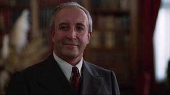 Movie still from “Being There” (1979), directed by Hal Ashby – An older man wearing a suit and tie in front of a book shelf; Close Up shot, Low angle