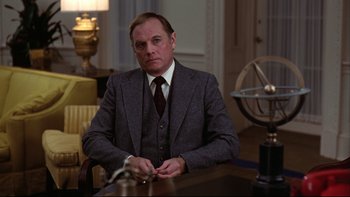 Movie still from “Being There” (1979), directed by Hal Ashby – A man sitting at a table wearing a suit and tie; Medium shot, Low angle