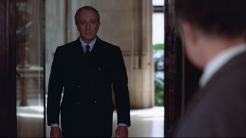 Movie still from “Being There” (1979), directed by Hal Ashby – A man in a suit and tie standing in front of a door; Medium shot, Over the shoulder angle