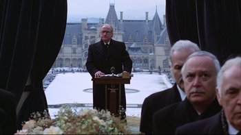 Movie still from “Being There” (1979), directed by Hal Ashby – An older man in a black suit standing at a podium in front of an old castle; Medium shot, Over the shoulder angle