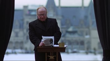 Movie still from “Being There” (1979), directed by Hal Ashby – An older man standing at a podium reading a paper; Medium shot, Low angle