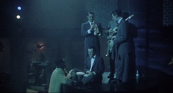 Movie still from “Bell, Book and Candle” (1976), directed by Hy Averback – A group of men in suits and ties playing musical instruments; Wide shot, High angle