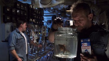Movie still from “Below” (2002), directed by David Twohy – A man looking at a fish in a jar in a room; Medium shot, Over the shoulder angle