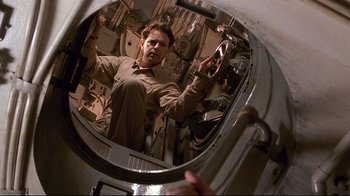 Movie still from “Below” (2002), directed by David Twohy – A man standing in front of a round mirror; Medium shot, Low angle