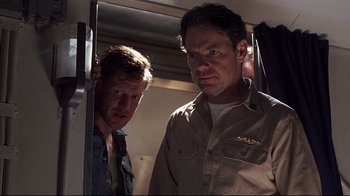 Movie still from “Below” (2002), directed by David Twohy – Two men standing next to each other on a train; Medium shot, Low angle