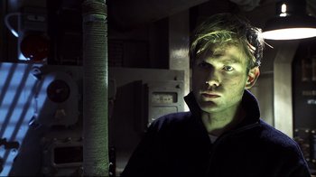 Movie still from “Below” (2002), directed by David Twohy – A young man is standing in a dark room; Close Up shot, High angle