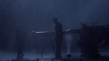 Movie still from “Below” (2002), directed by David Twohy – A man standing in the rain next to a table; Wide shot, Low angle