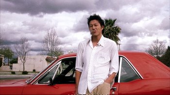 Movie still from “Better Luck Tomorrow” (2002), directed by Justin Lin – A man standing in front of a red car; Medium shot, Low angle