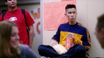 Movie still from “Better Luck Tomorrow” (2002), directed by Justin Lin – A man sitting on the ground with a bag of popcorn in front of him; Medium shot, Over the shoulder angle