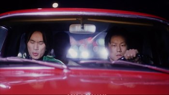 Movie still from “Better Luck Tomorrow” (2002), directed by Justin Lin – Two people in a red car with lights in the background; Medium shot, Low angle