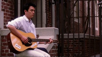 Movie still from “Better Luck Tomorrow” (2002), directed by Justin Lin – A man sitting on a bench playing an acoustic guitar; Medium shot, High angle