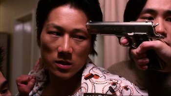 Movie still from “Better Luck Tomorrow” (2002), directed by Justin Lin – A man is getting his hair cut by a man with a gun; Close Up shot, Over the shoulder angle