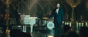 Movie still from “Beyond the Sea” (2004), directed by Kevin Spacey – A man singing into a microphone in front of a group of people; Wide shot, Over the shoulder angle