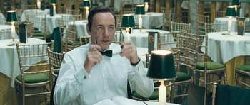 Movie still from “Beyond the Sea” (2004), directed by Kevin Spacey – A man sitting at a table holding a pair of scissors in front of his face; Close Up shot, Over the shoulder angle